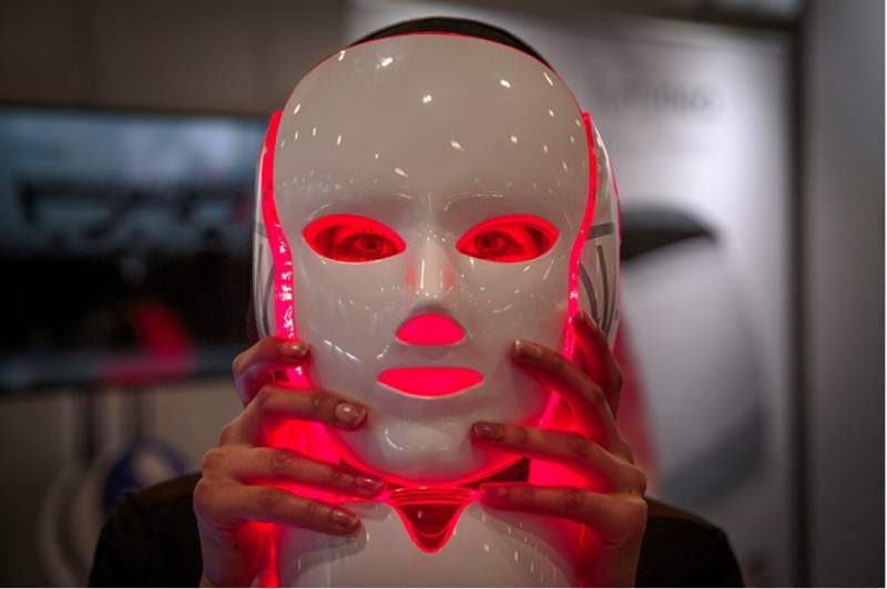 Close-up of a white, shiny face mask, emitting red light onto the face in front of which it is being held..